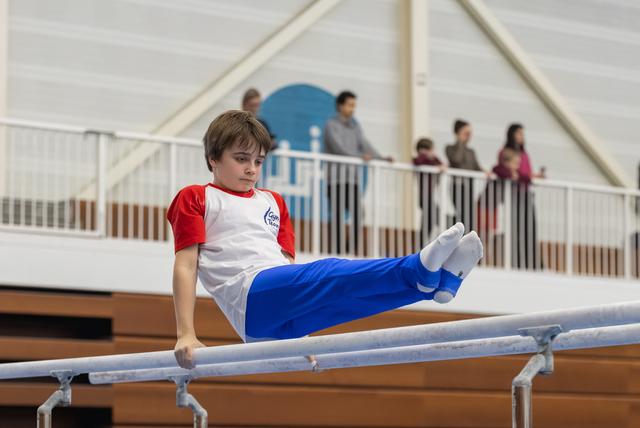 Young gymnast performing a leg extension on parallel bars, displaying focused concentration in training facility