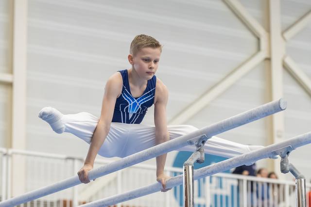 Young male gymnast performs L-sit position on parallel bars, displaying focused concentration during routine