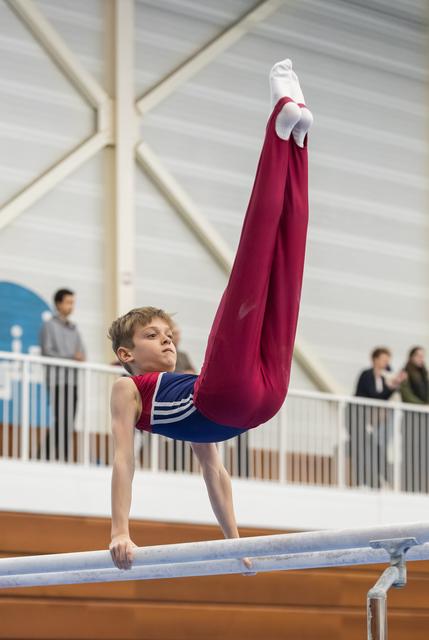 Young gymnast performing an L-sit on parallel bars with extended legs, displaying intense focus and strength in the indoor facility
