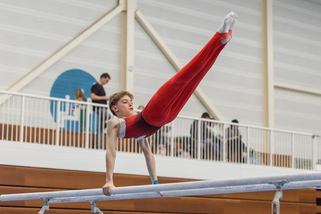 Young male gymnast performing an L-sit hold on parallel bars, demonstrating strength and focus in a training facility