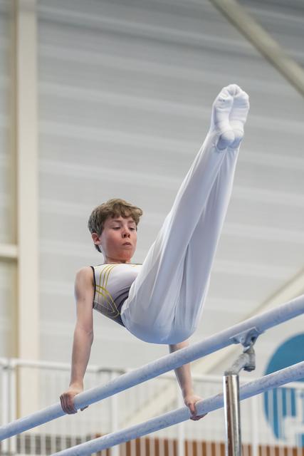 Young gymnast performing leg extension on parallel bars with focused expression during training routine