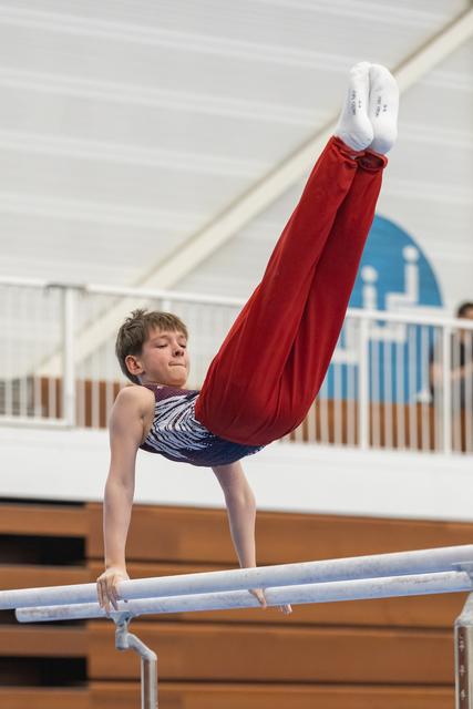 Young gymnast performing handstand with legs extended vertically on parallel bars in indoor training facility