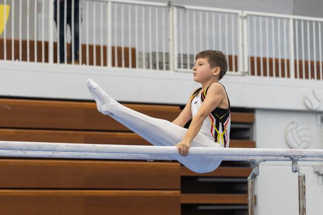 Young gymnast performing a straight leg hold on parallel bars, demonstrating strength and focus during training