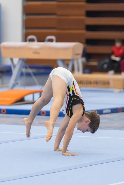 Young gymnast executes a deep backbend during floor routine, showcasing flexibility with head lowered and legs extended