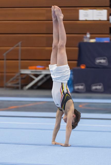Young gymnast executes a controlled handstand with straight legs on blue floor mat in training facility