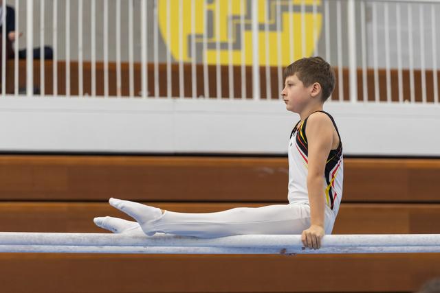 Young gymnast executing an L-sit hold on parallel bars, demonstrating strength and focused concentration in the gym