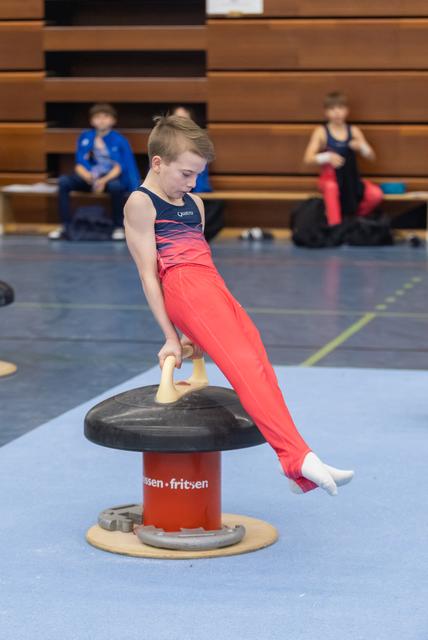 Young gymnast in red uniform executes a horizontal circle position on pommel mushroom apparatus during training session