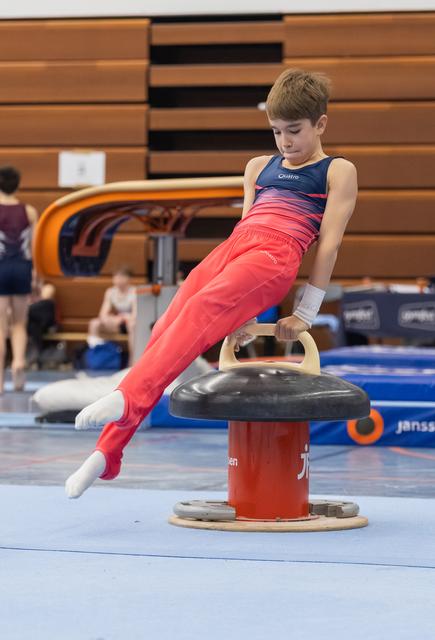 Young gymnast in red pants and blue leotard performing a strength hold on the pommel horse mushroom apparatus