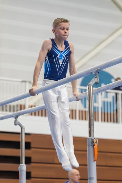 Young gymnast in blue leotard concentrates while performing on parallel bars in indoor gymnasium