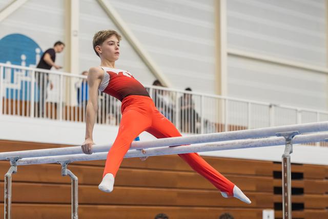 Young gymnast executing a horizontal hold on parallel bars, displaying strength and concentration in a training facility