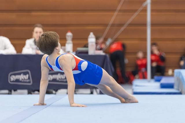 Young gymnast in blue leotard performs plank position on floor mat, demonstrating strength and form during routine