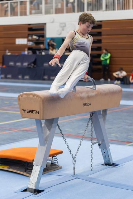 Young gymnast executes a scissor movement on pommel horse, demonstrating control and concentration during training session