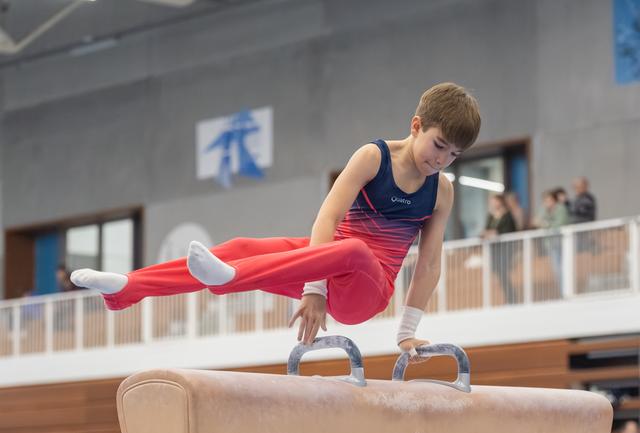 Young gymnast demonstrates strength and focus on pommel horse, executing a horizontal hold with legs extended