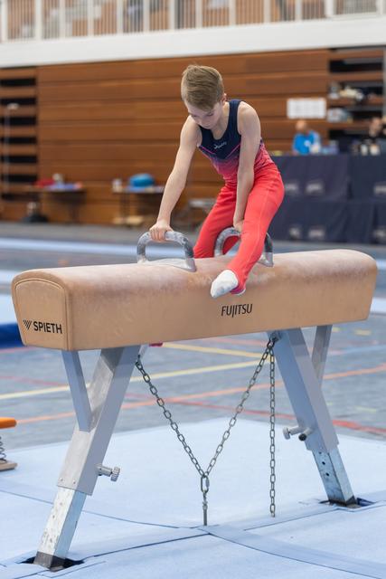 Young gymnast in gradient leotard executes a move on the pommel horse, demonstrating focus and control in the gym.