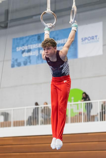 Young gymnast demonstrates strength on rings apparatus, holding position with focused expression during routine