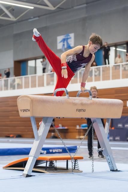 Young male gymnast performing a handstand with elevated legs on pommel horse during training at indoor gymnastics facility