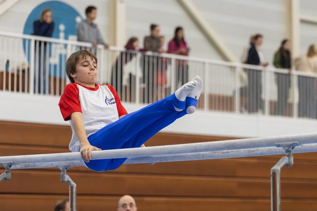 Young gymnast executes a horizontal hold on parallel bars with focused concentration while spectators watch from above
