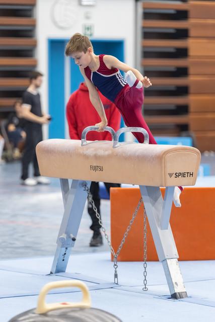 Young male gymnast in maroon and blue performs a pommel horse routine with focused concentration in training facility