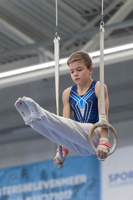 Young male gymnast holds a horizontal position on still rings, displaying intense concentration during his routine
