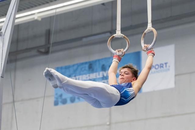 Young gymnast demonstrates strength position on still rings, body extended horizontally with focused concentration