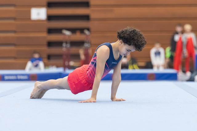 Young gymnast holds a plank position during floor routine, demonstrating strength and focus on competition mat