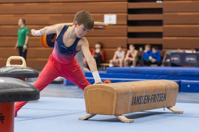 Young gymnast in gradient leotard performs support position on pommel horse during training session in gymnasium