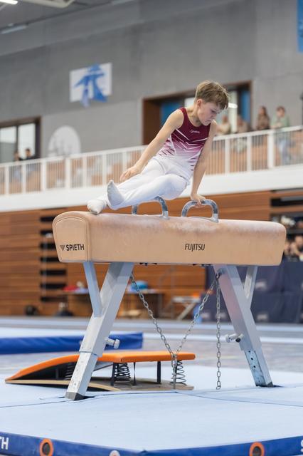 Young gymnast performs a scissor move on the pommel horse, demonstrating strength and control during his routine