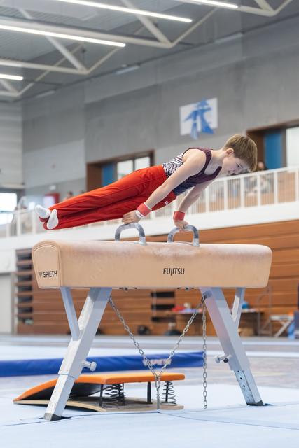 Young gymnast performing horizontal hold on pommel horse with extended body, demonstrating strength and control in training facility