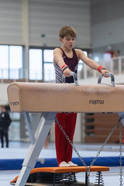 Young gymnast gripping pommel horse handles during practice, focused and determined in indoor training facility