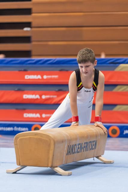 Young gymnast in white leotard performs on pommel horse, focused expression, hands gripping apparatus in indoor gym