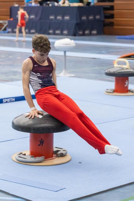 Young gymnast in red pants and patterned leotard practices on mushroom apparatus, legs extended during training routine