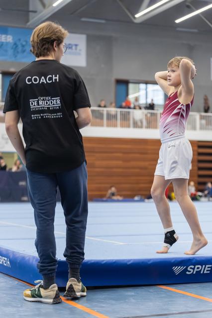 Young gymnast practicing her routine on the balance beam under the watchful eye of her coach at the training facility