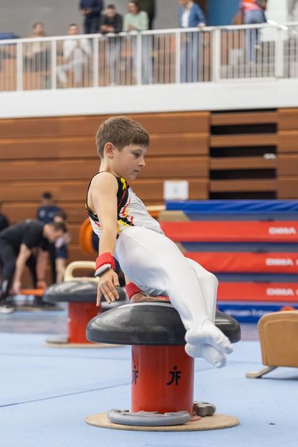 Young gymnast in white and yellow uniform concentrates while practicing on the pommel horse during training