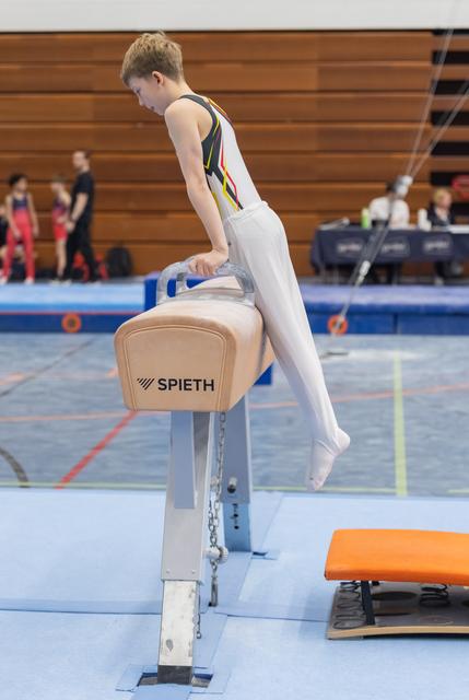 Young gymnast in white and green leotard grips pommel horse handles, focused and ready to begin routine in gymnasium