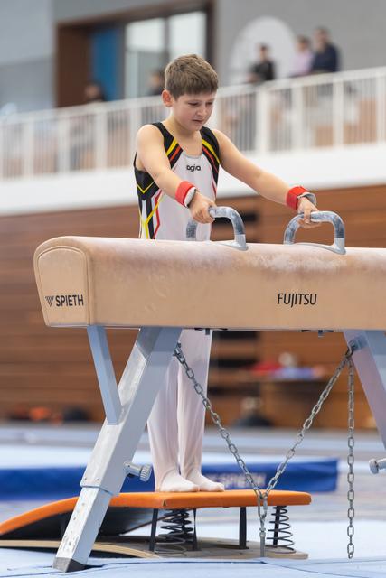 Young gymnast in black and yellow leotard concentrates while gripping pommel horse handles before his routine