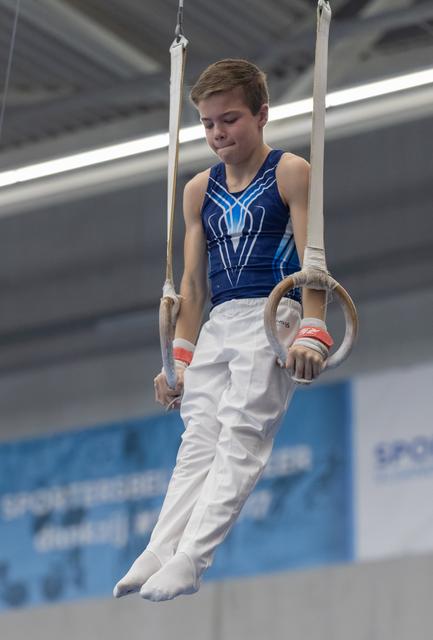 Young gymnast on rings apparatus displaying focus and determination during routine in indoor training facility