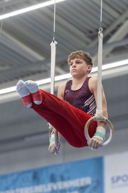 Young male gymnast performing L-sit position on rings, displaying intense focus and controlled strength in gymnasium