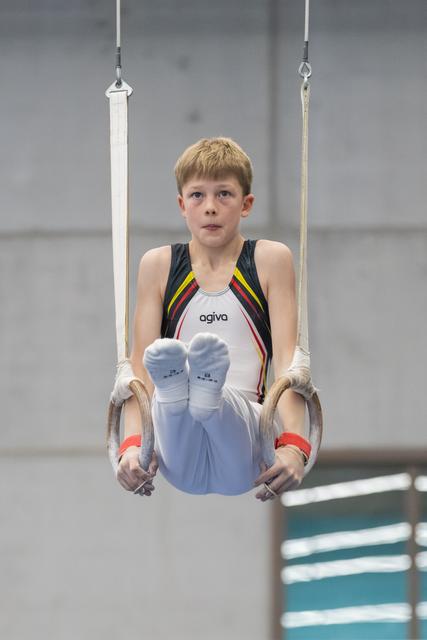 Young gymnast performing L-sit on rings, displaying intense concentration and controlled form during routine