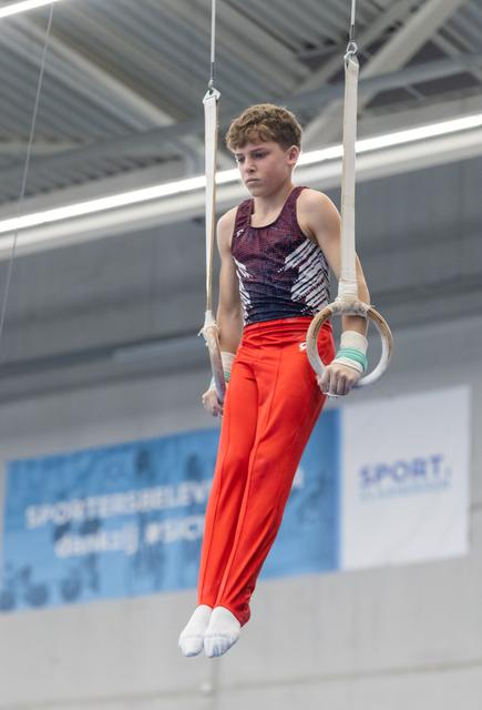Young male gymnast performing on rings apparatus in training facility, displaying concentration and strength
