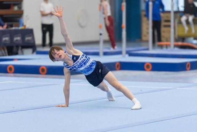 Young gymnast in blue gradient leotard performs a side plank with raised arm during floor routine at gymnastics meet
