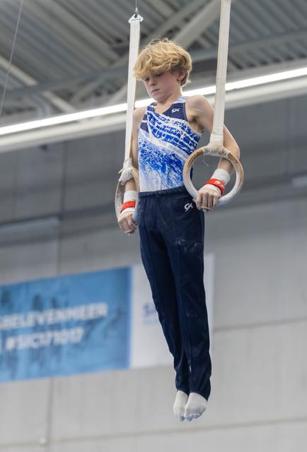 Young gymnast performing on still rings, demonstrating control and focus with bent arms in indoor training facility