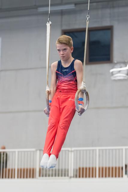 Young gymnast in coral outfit maintains focused straight-arm support position on still rings during training session