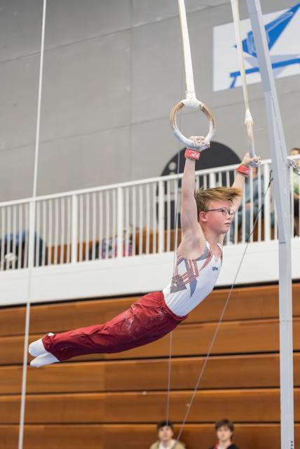 Young gymnast performing a horizontal hold on still rings, displaying focus and strength during his routine in an indoor gym