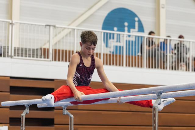 Young gymnast performing a straddle hold on parallel bars, focused and concentrated in training gym