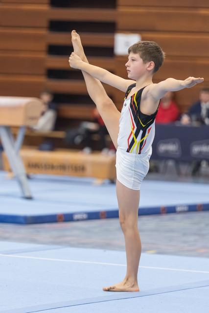 Young gymnast performs vertical split balance on floor, demonstrating flexibility and control during routine