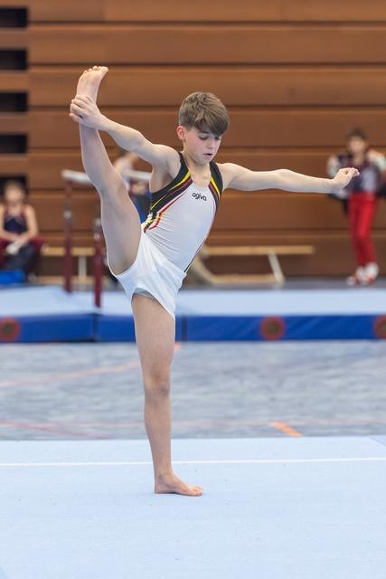 Young gymnast performs impressive vertical split balance on floor, demonstrating exceptional flexibility in white German team leotard