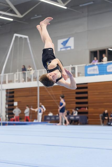 Gymnast performing a backflip mid-air during floor routine at indoor competition, body fully inverted with focused expression