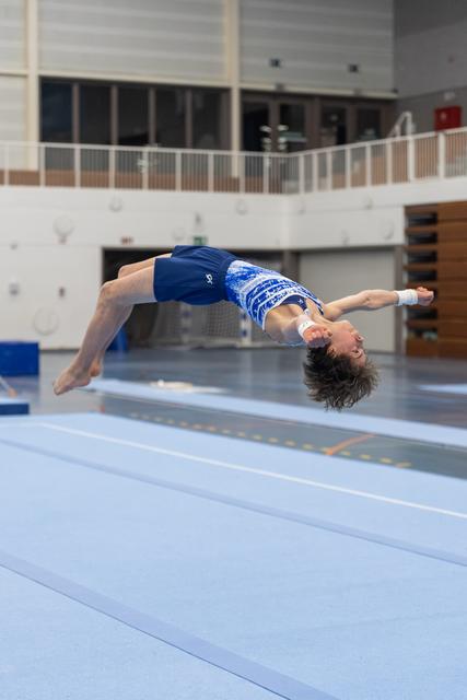Female gymnast performing a backflip on floor exercise, body arched mid-air in training facility