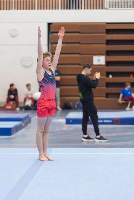 Young gymnast completes floor routine with arms raised high, showing concentration and poise in gymnasium