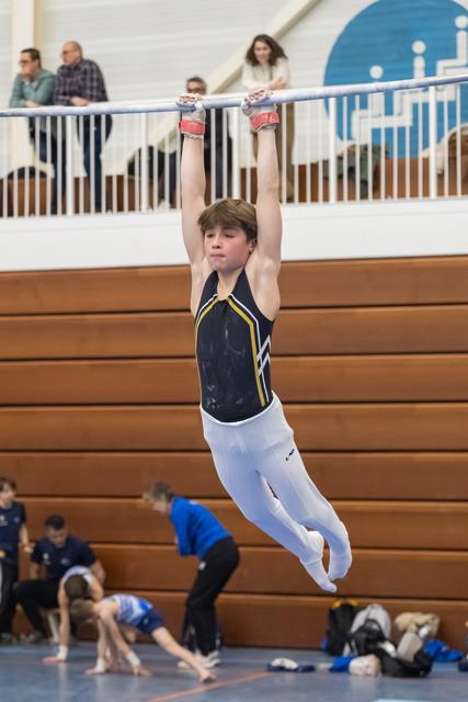Young gymnast hanging from high bar with arms extended, demonstrating strength during floor routine in gymnasium
